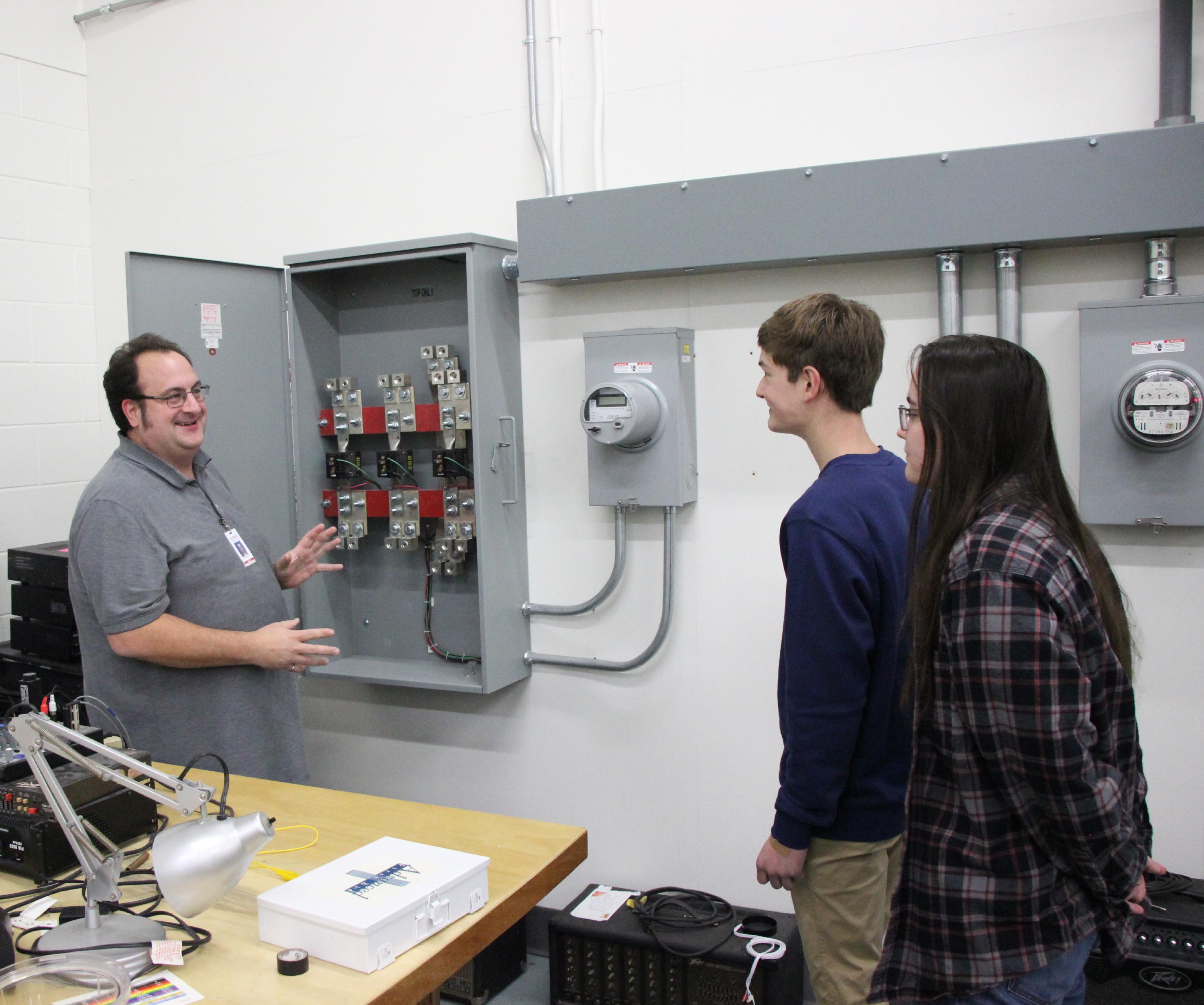 Instructor Wes Repke shows something on an electrical panel to two students